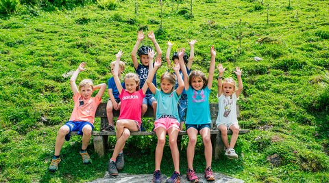 Kinder sitzen auf Bank und strecken Hände in die Höh